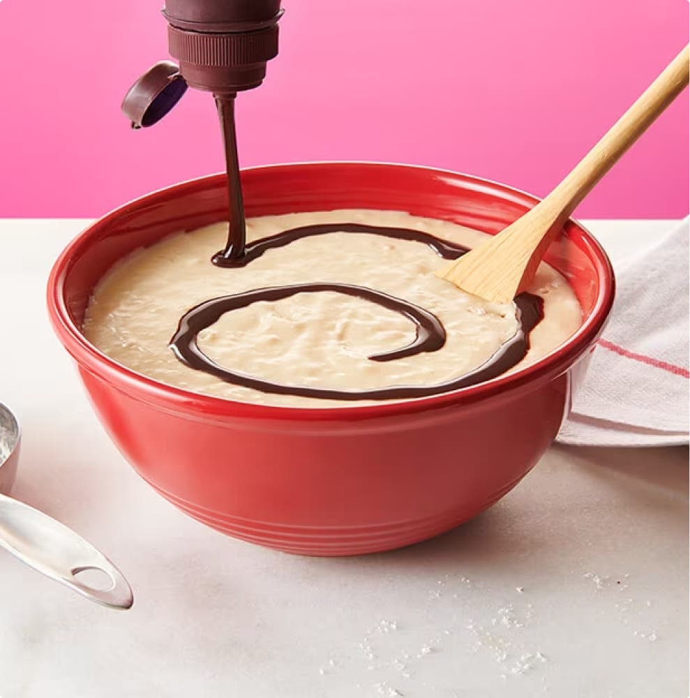 pouring hersheys chocolate syrup on top of pancake batter in mixing bowl