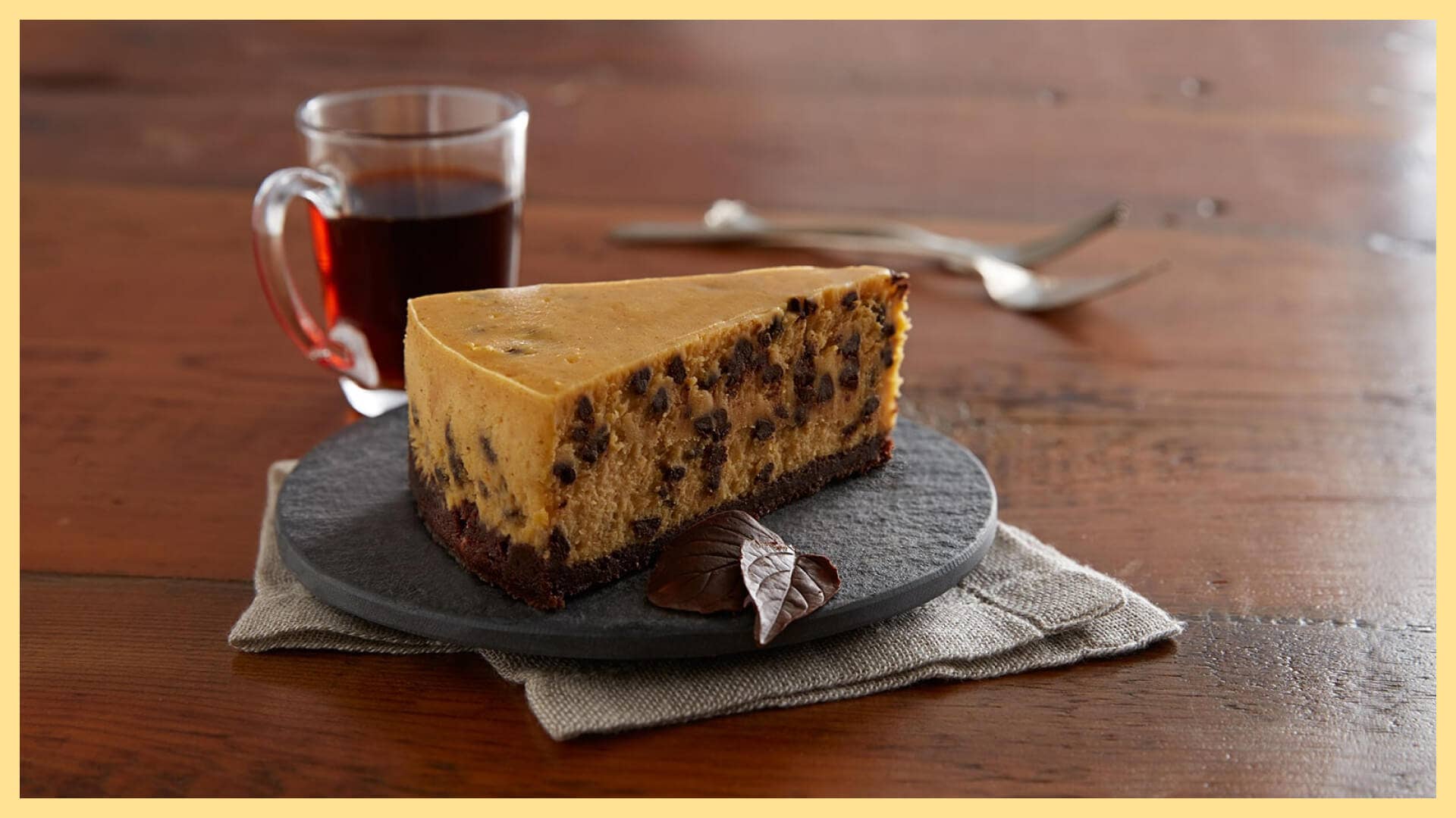 slice of chocolate chip pumpkin cheesecake with a mug of coffee and garnished with chocolate leaves