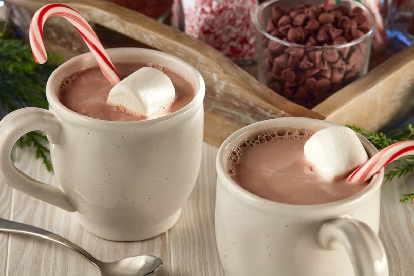 two mugs of hot chocolate next to a tray of garnishes