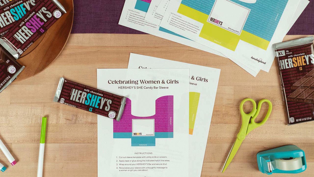 DIY candy bar sleeve craft shown with scissors, tape, markers and candy bars